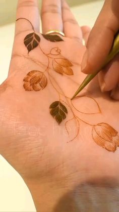 someone is doing something on their hand that has leaves and flowers painted on the palm