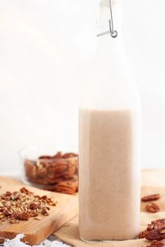 a glass bottle filled with milk sitting on top of a wooden cutting board next to nuts