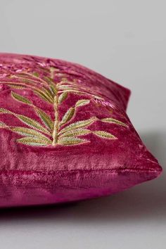 a close up of a pink pillow on a gray surface with gold embroidered leaves and vines