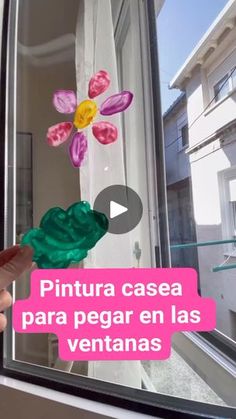 a person holding a fake flower in front of a window with the words pintura casea para pegar en las ventanas