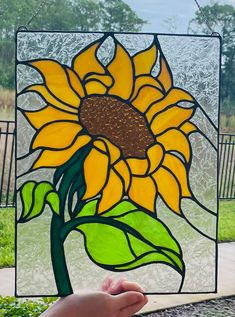 a hand holding up a stained glass window with a sunflower on it's side