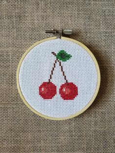 a cross - stitch pattern with two cherries hanging from it's hoop on a piece of fabric