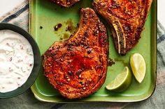 two pieces of meat on a green plate with sour cream and lime wedges next to it