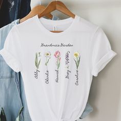 "Welcome to our Etsy listing for the \"Grandma's Garden\" personalized T-Shirt! This beautiful shirt is the perfect way to honor your children or grandchildren and their birth month flowers. This is a perfect gift for Grandma! The front of the tee features the phrase \"Grandma's Garden\" in a charming and elegant font. Beneath the phrase, we will add the names of your children or grandchildren in a lovely script font. Each name will be underneath their birth month flower, delicately illustrated with vibrant colors. Our \"Grandma's Garden\" T-shirt is the ideal gift for any proud grandma who loves to keep her loved ones close. This shirt will be a beautiful addition to any wardrobe and is sure to be cherished for generations to come. Thank you for considering our \"Grandma's Garden\" person Spring Short Sleeve Shirt With Name Print, Spring Gift Shirt With Custom Print, Spring Graphic Tee Shirt With Name Print, Spring T-shirt With Name Print In Relaxed Fit, Spring Relaxed Fit T-shirt With Name Print, Grandma's Garden, Mom Tshirt, Custom Tee, Elegant Font