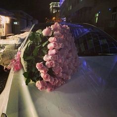 pink flowers are placed on the hood of a white car at night with buildings in the background