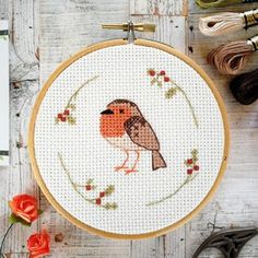 a cross stitch bird sitting on top of a wooden table next to scissors and thread