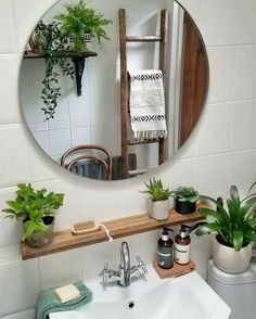 there is a mirror above the sink in this bathroom with plants and towels on it