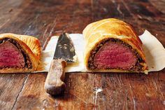 a piece of meat in a pastry sitting on top of a wooden table next to a knife