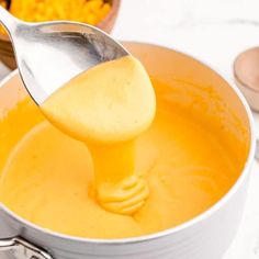 a ladle full of orange liquid being poured into a pot with other ingredients in the background