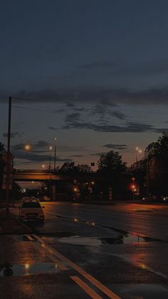 a city street at night with cars parked on the side of the road and traffic lights in the background