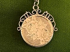 "Description: Beautiful round vintage 10K yellow gold fob locket necklace. This antique fob locket features an etched design of two flowers surrounded by leaves on the front. The background behind the roses is a textured surface. There are etched notches on the outer rim of the rose design all the way round the round locket front. The back side is plain with no etched design. This antique locket has a decorative and ornate scroll openwork frame around the top that goes downward to the mid sectio Vintage Necklace With Hallmark And Round Pendant, Vintage Necklace With Round Pendant And Hallmark, Vintage Hallmark Round Pendant Necklace, Victorian Medallion Jewelry With Hallmark, Victorian Rose Gold Medallion Necklace, Victorian Necklaces With Charms For Anniversary, Victorian Hallmark Jewelry For Memorial, Victorian Rose Gold Collectible Necklace, Victorian Memorial Jewelry With Hallmark