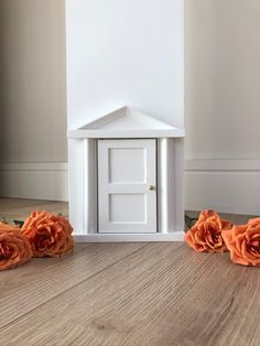 there are three fake flowers on the floor next to a dollhouse door and small house