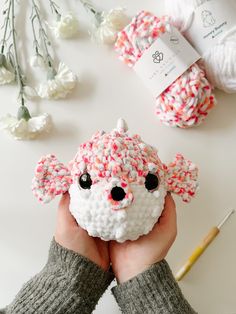 someone is holding up a crocheted sheep ornament in front of yarn balls