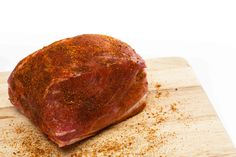 a piece of meat sitting on top of a wooden cutting board covered in seasoning