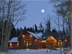 a house is lit up with christmas lights in the snow at night and surrounded by trees