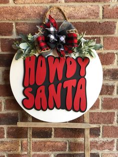 a sign that says howdy santa hanging on a brick wall