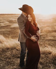 a pregnant woman in a red dress and cowboy hat hugging her husband