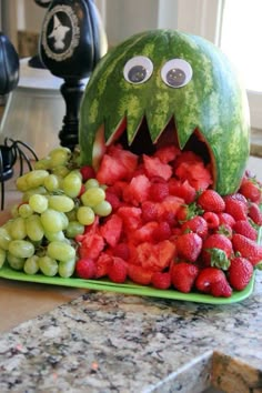 a watermelon shaped like a monster with grapes and strawberries in front of it