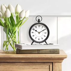 a clock sitting on top of a wooden table next to a vase with white flowers