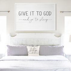 a bed with blue and white striped sheets, pillows and a sign above it that says give it to god and stay