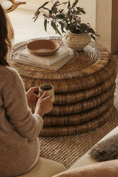 a woman sitting on a couch holding a cup in front of a stack of books