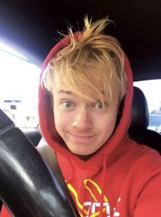 a young man in a red hoodie sitting in a car wearing a mcdonald's sweatshirt