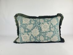 a blue and white flowered pillow with black fringe on the bottom, against a white background