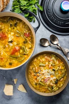 two bowls filled with vegetable soup next to spoons