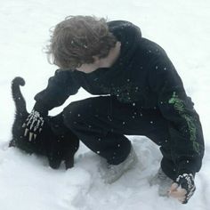 a young boy playing in the snow with his black dog, who is looking down at him