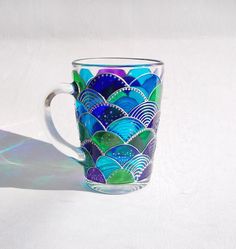 a colorful glass mug sitting on top of a white table next to a shadow from the sun