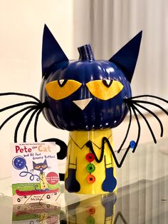 a blue and yellow cat figurine sitting on top of a glass table next to a book