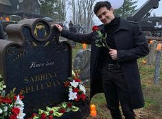 a man standing next to a grave with flowers on it