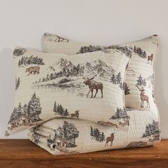 two pillow cases with moose and mountain scenes on them, sitting on a wooden shelf