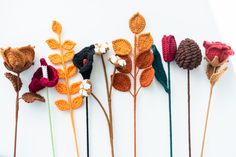 crocheted flowers are arranged in rows on a white surface, with leaves and buds attached to them