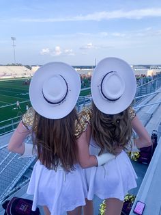 two girls in white dresses and cowboy hats standing on the bleachers at a football game