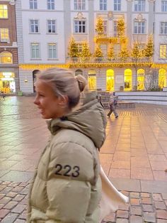 a woman walking down the street in front of a building with christmas lights on it