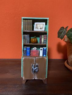 a miniature book shelf with books on it next to a potted plant