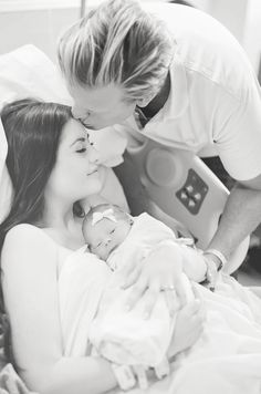 a man kisses the forehead of a woman as she lays in bed with her baby