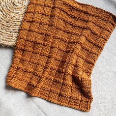 an orange knitted blanket sitting on top of a bed next to a wicker basket