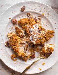 a white plate topped with a piece of cake covered in pecans and powdered sugar