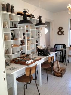 a room filled with lots of white shelves and wooden chairs next to a table covered in books