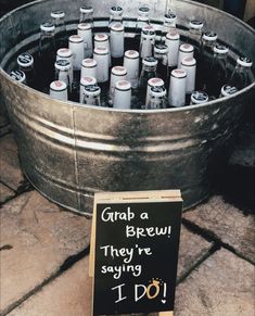 a metal bucket filled with lots of bottles next to a sign that says grab a brew they're saying i do