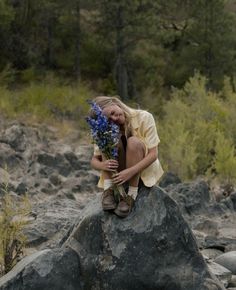 a woman sitting on top of a rock holding flowers