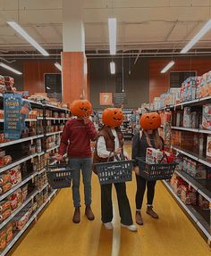 three people wearing pumpkin hats in a grocery store aisle with baskets full of food on the shelves