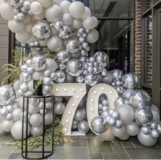 a large number seventy surrounded by silver and white balloons