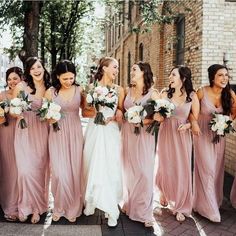 a group of women standing next to each other in front of a brick building holding bouquets