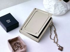 an open book sitting on top of a white table next to a box and necklace