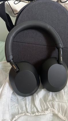 two black headphones sitting on top of a white bed next to a gray pillow