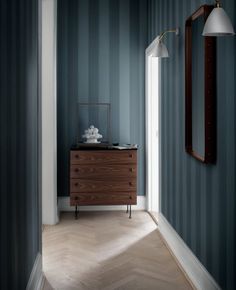 an empty hallway with blue walls and wooden furniture in the corner, along with a mirror on the wall