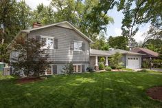 a large gray house sitting in the middle of a lush green field next to trees